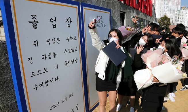 Middle school grads take photos in front of large diploma